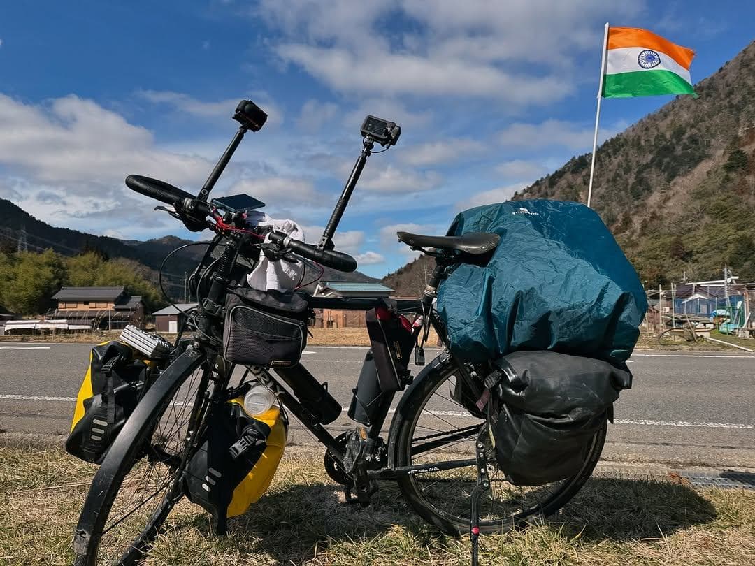 Ranjith's loaded touring bicycle by the roadside with the Indian flag, mountains behind